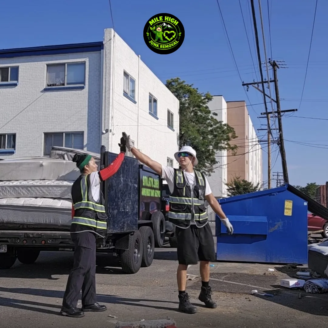 Two Mile High Junk Removal crew members high-fiving next to their trailer during a job in Denver